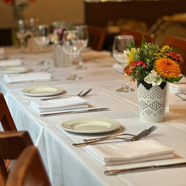 A long dining table set with white tablecloths, plates, silverware, and floral centerpieces at Paradiso's.
