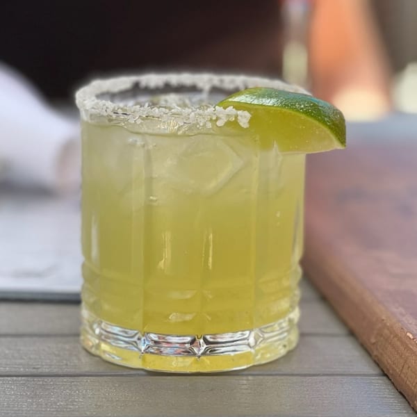 A refreshing Paradiso's margarita with a salted rim and lime wedge on a wooden table.