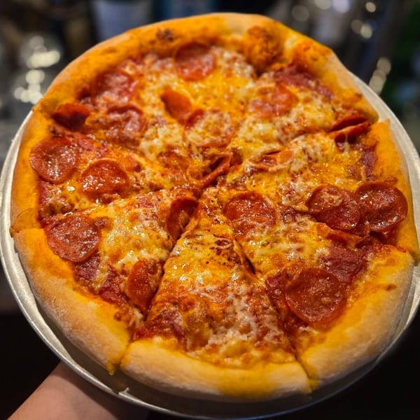 A freshly baked, sliced pepperoni pizza with melted cheese on a metal tray from Paradiso's Restaurant.