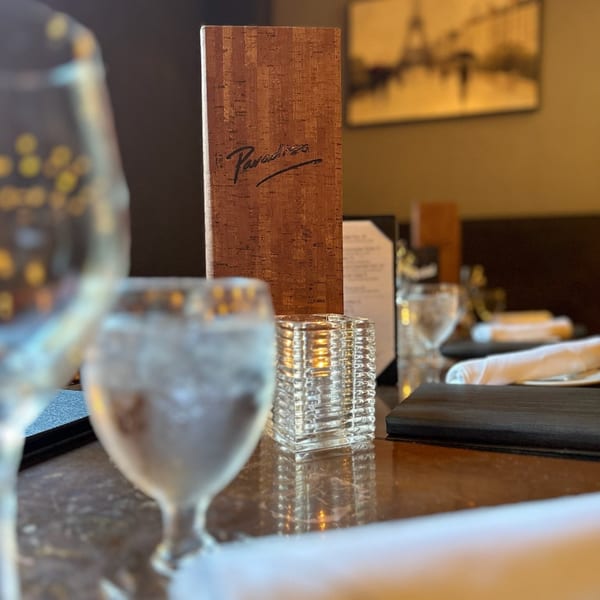 A Paradiso's Restaurant menu stands on a table with water glasses and a candle holder.