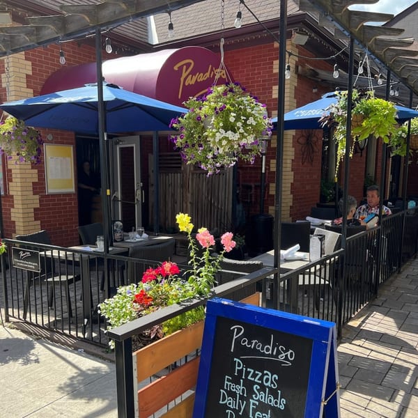 Paradiso's Restaurant outdoor patio with blue umbrellas, hanging flower baskets, and a chalkboard sign.