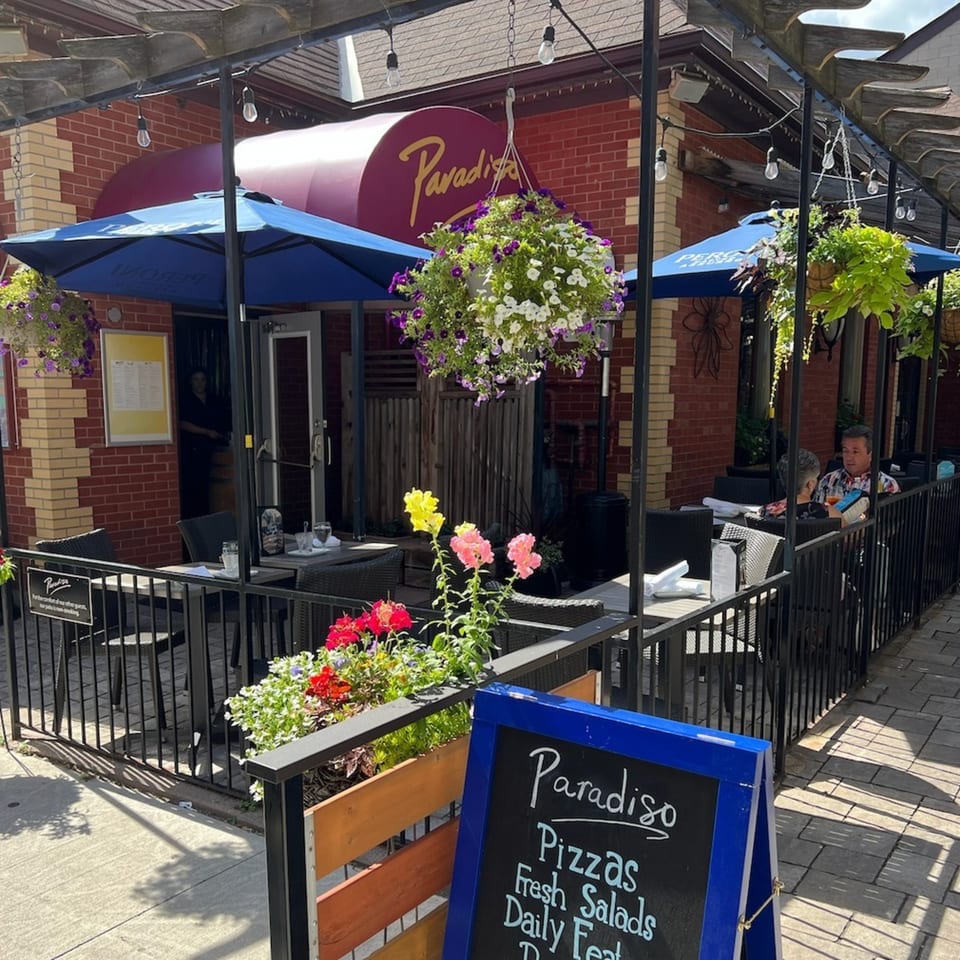 Paradiso's Restaurant outdoor patio with blue umbrellas, hanging flower baskets, and a chalkboard sign.