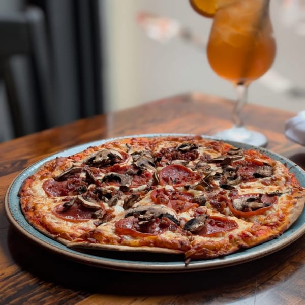 Pepperoni and mushroom pizza on a blue plate with an orange cocktail in the background.