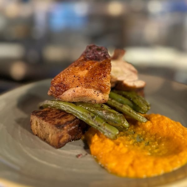 Seared chicken with green beans and orange puree on a gray plate at Paradiso's Restaurant.
