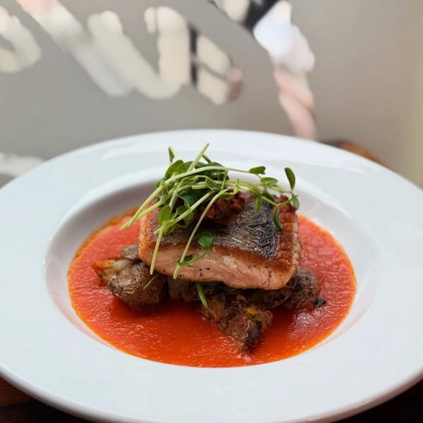 Pan-seared salmon with crispy skin, microgreens, roasted potatoes, and a vibrant red sauce on a white plate.