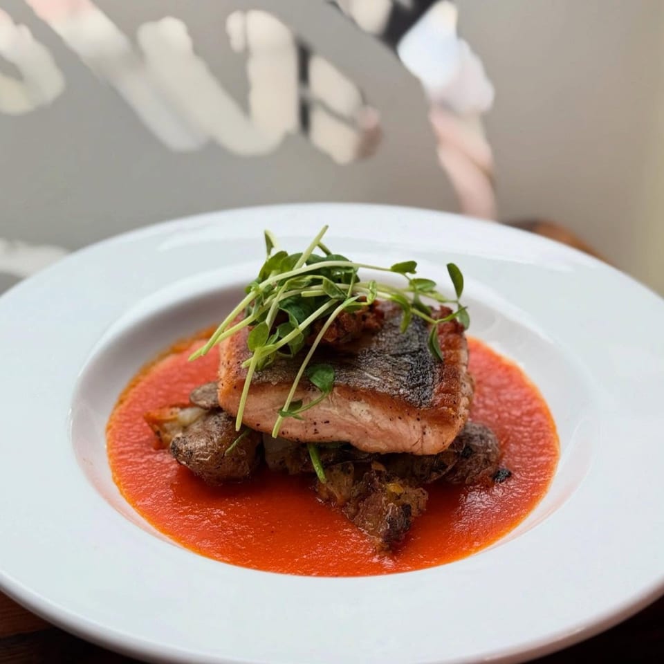 Pan-seared salmon with crispy skin, microgreens, roasted potatoes, and a vibrant red sauce on a white plate.