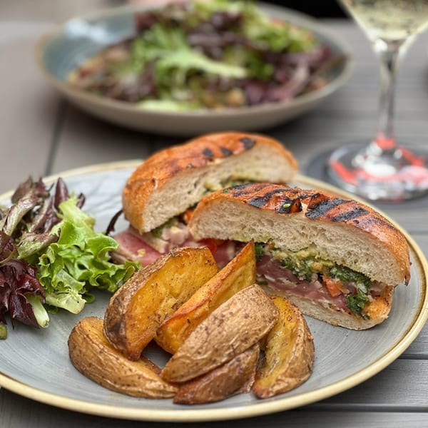 A Paradiso's sandwich with grilled bread, pesto, prosciutto, and avocado, served with potato wedges and salad.
