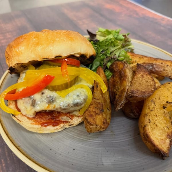 A Paradiso's burger with melted cheese, peppers, and pickles, served with potato wedges and salad.