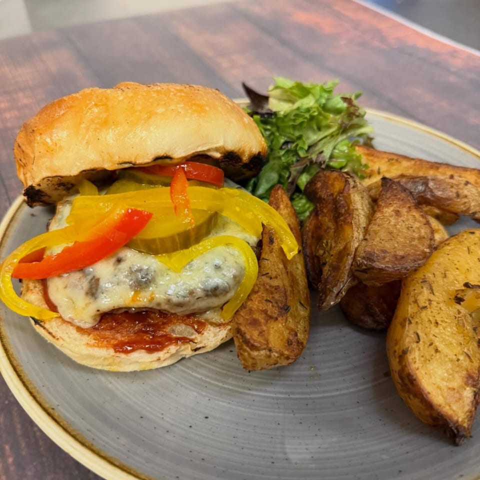 A Paradiso's burger with melted cheese, peppers, and pickles, served with potato wedges and salad.