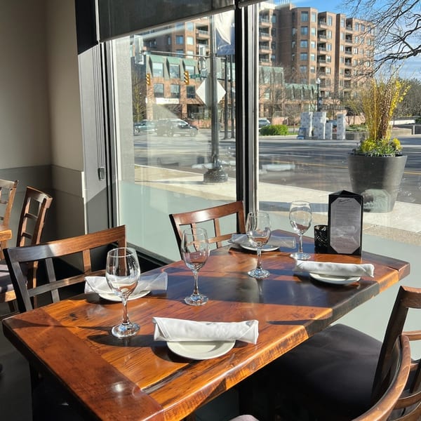 A Paradiso's Restaurant dining table set with wine glasses and plates, bathed in sunlight from a large window.