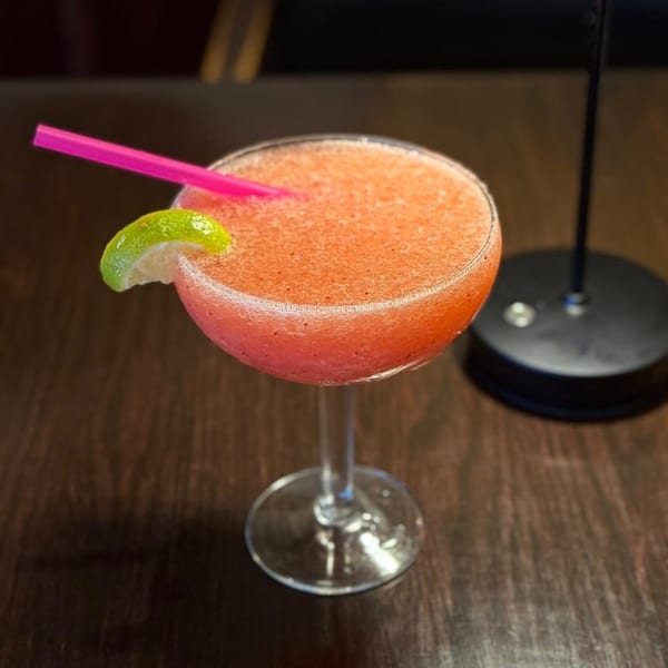 A vibrant pink frozen drink with a lime wedge and pink straw sits on a dark wooden table.