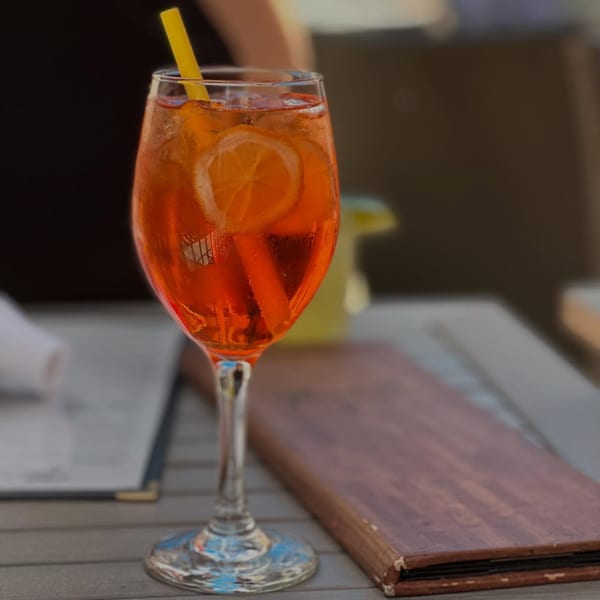 A vibrant orange Aperol Spritz cocktail with a lemon slice and yellow straw on a wooden table.