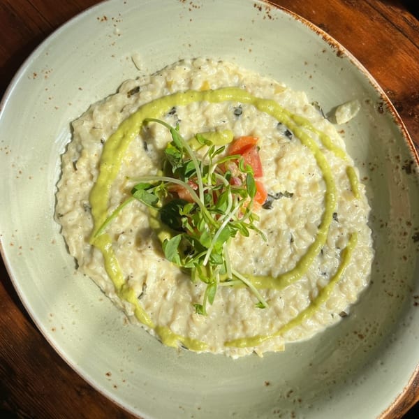Creamy Italian risotto with green sauce, microgreens, and diced tomatoes in a light-colored bowl.