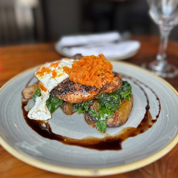 Grilled salmon with spinach, potatoes, creamy sauce, and caramelized onions on a plate.