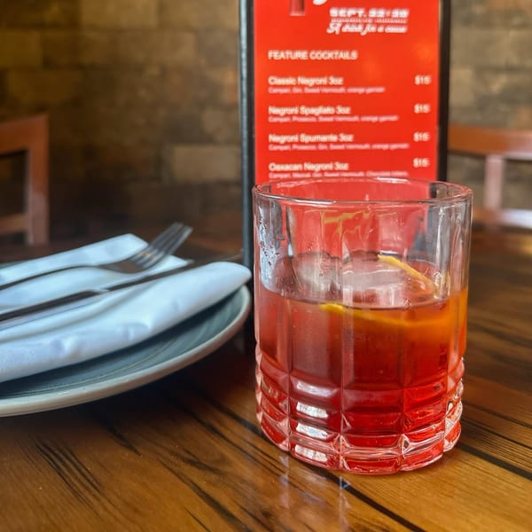 A Paradiso's Restaurant cocktail, possibly a Negroni, with a menu and place setting on a wooden table.