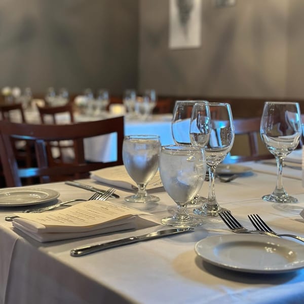 A set table at Paradiso's Restaurant with white tablecloths, menus, plates, and glasses.