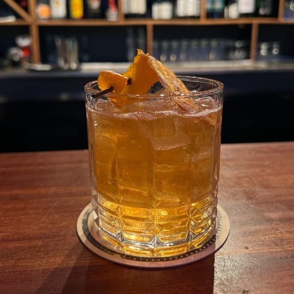 A Paradiso's Restaurant cocktail with ice and an orange peel garnish on a wooden bar.