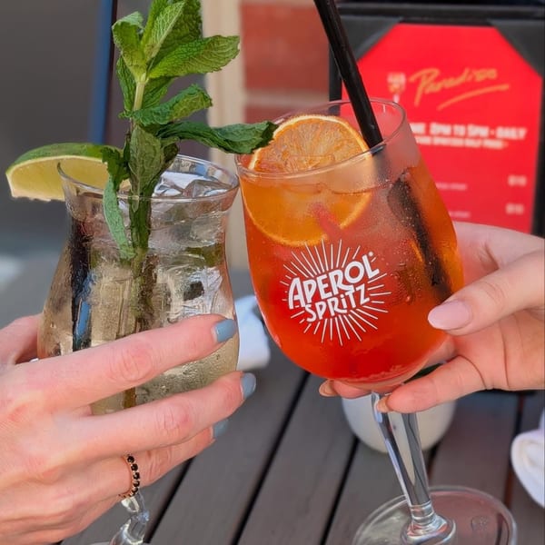 Two hands holding cocktails, one Aperol Spritz, one clear drink with mint and lime.
