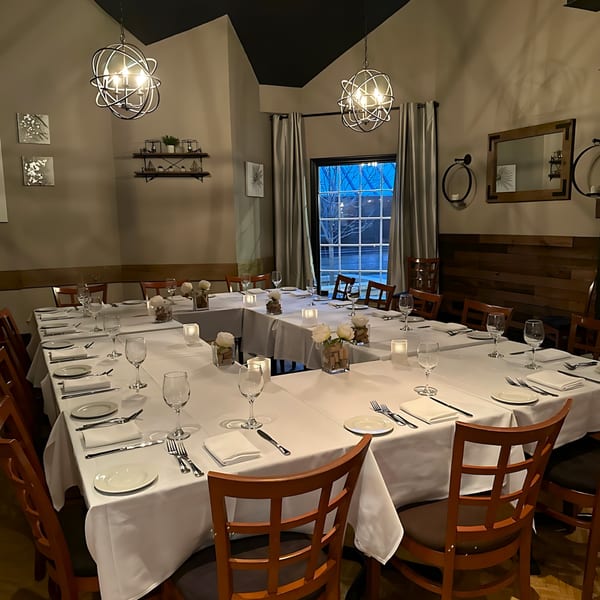 A private dining room at Paradiso's Restaurant with U-shaped tables set with white linens and place settings.