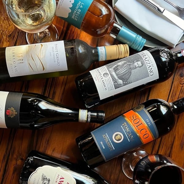 Assortment of Italian red, white, and rosé wine bottles with glasses on a wooden table.