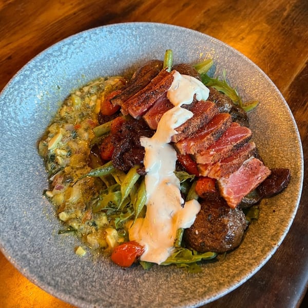 Seared tuna slices with creamy sauce, roasted potatoes, green beans, and cherry tomatoes on a plate.