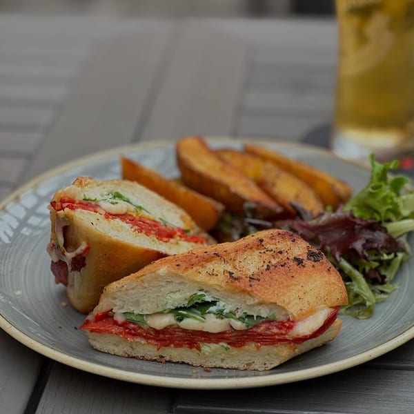 A Paradiso's Italian sandwich with melted cheese, pepperoni, and greens, served with potato wedges and salad.