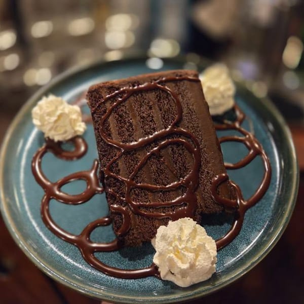 A slice of Paradiso's chocolate cake with chocolate drizzle and whipped cream on a blue plate.