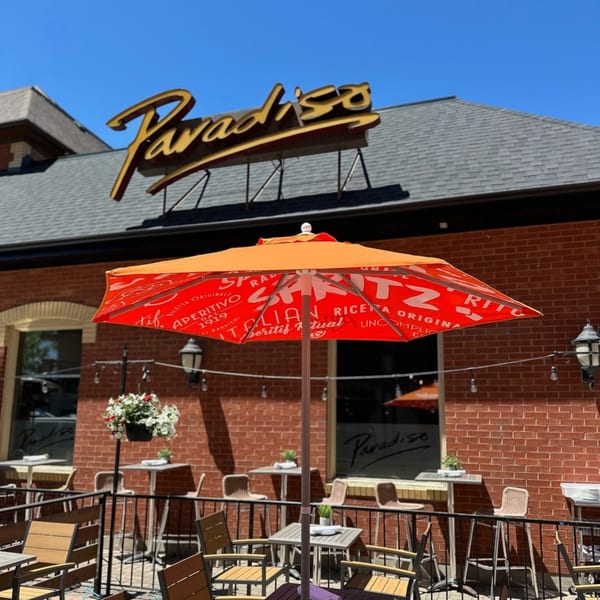 Paradiso's Restaurant exterior with a large orange umbrella on the patio, tables, and chairs.