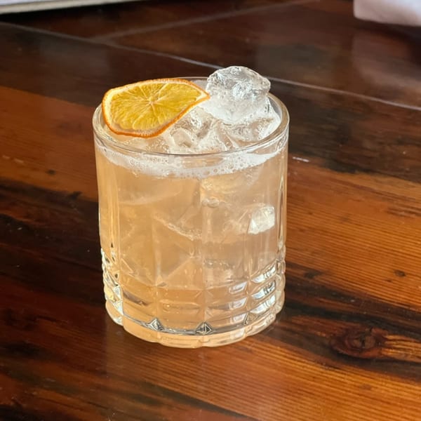 A refreshing cocktail with ice and an orange slice, served in a textured glass on a wooden table.