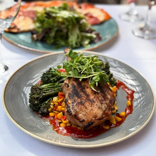 Grilled pork chop with broccolini, corn, peppers, and red sauce on a gray plate.