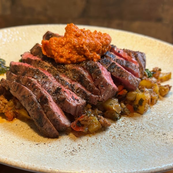Sliced steak with a vibrant red sauce on top, served over a bed of roasted vegetables.
